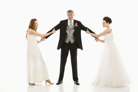 Caucasian and Asian brides pulling on Caucasian groom's arms.の写真素材