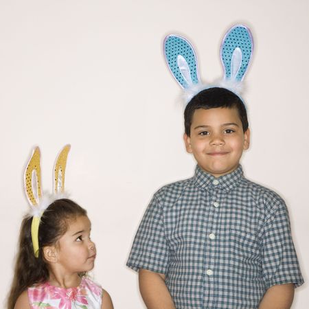 Hispanic girl looking up at Hispanic boy both wearing bunny ears.の写真素材