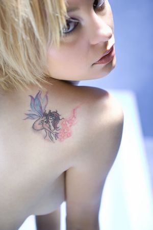 Portrait of  attractive young adult Caucasian blond woman with tattoo looking over shoulder making eye contact.の写真素材