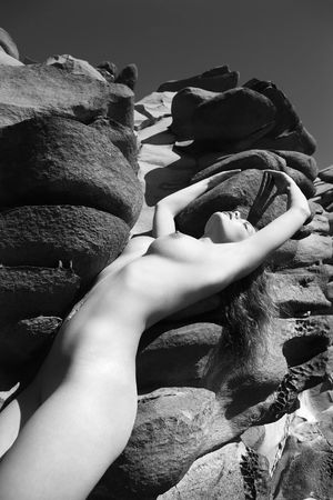 Sexy Caucasian young adult woman with eyes closed standing nude against rocks at Maui coast with arms stretched over head.の写真素材
