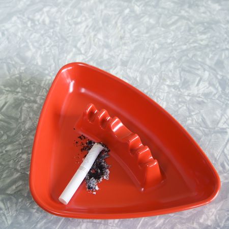 Still life of red plastic vintage ashtray containing cigarette butt and ashes.の写真素材