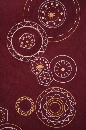 Close-up of maroon vintage fabric with white and yellow lines and shapes printed on polyester.