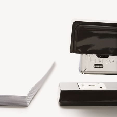 Close up of black stapler on white background with stack of paper.の写真素材