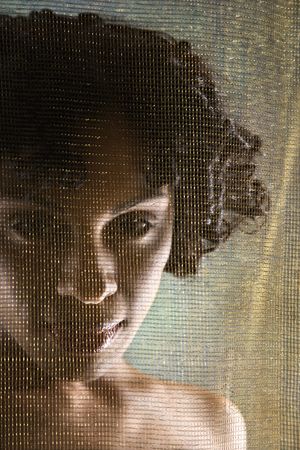  Hispanic woman looking at viewer from behind sheer fabric.