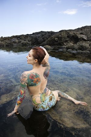 Back view of sexy topless tattooed Caucasian woman in bikini sitting in tidal pool in Maui, Hawaii, USA.の写真素材