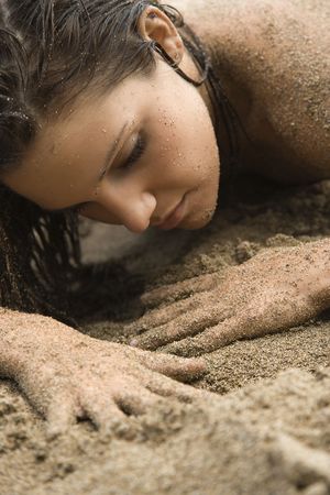 Head shot of Caucasian young adult  woman lying in sand.の写真素材
