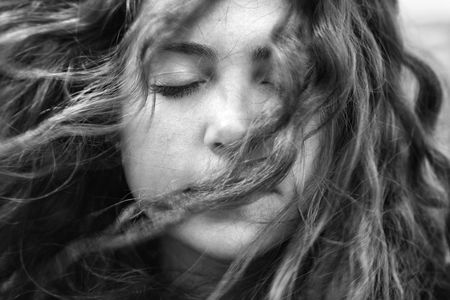 Young adult Caucasian female with hair blowing in face and eyes closed.の写真素材
