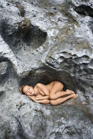 Young Asian nude woman sleeping in a crevice in a rock.の写真素材