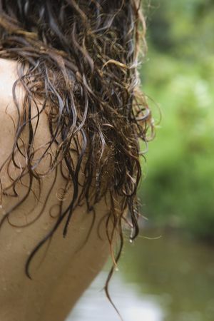 Back and long wet hair of Caucasian young adult woman by stream in lush green forest.の写真素材