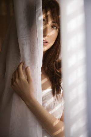 Portrait of pretty Caucasian young woman standing in sunlit curtains.の写真素材