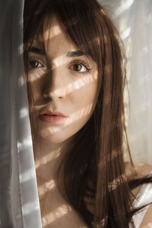 Portrait of pretty Caucasian young woman standing in sunlit curtains.の写真素材