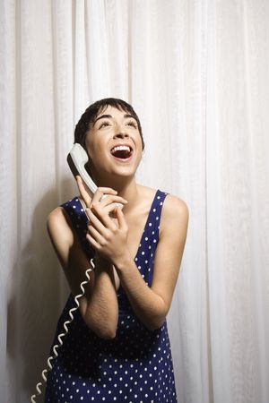 Pretty Caucasian young woman holding telephone receiver to ear and laughing.の写真素材