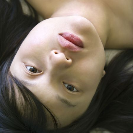 Head and shoulder portrait of pretty young Asian woman lying in bed making eye contact.の写真素材