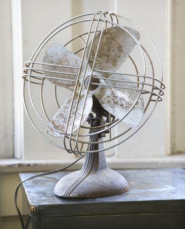 Retro style metal fan sitting on tabletop by window.の写真素材