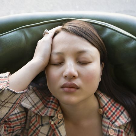 Pretty young Asian woman sitting in green chair with eyes closed.の写真素材