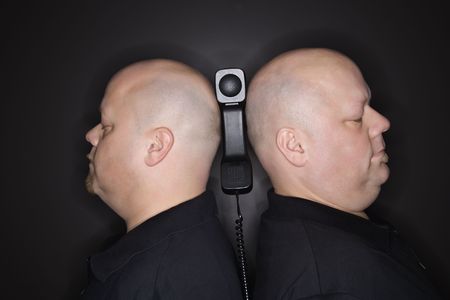 Caucasian mid adult identical twin men standing back to back with telephone balancing between them.