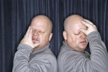 Caucasian bald identical twin men standing back to back and grimicing with hands to head.の写真素材