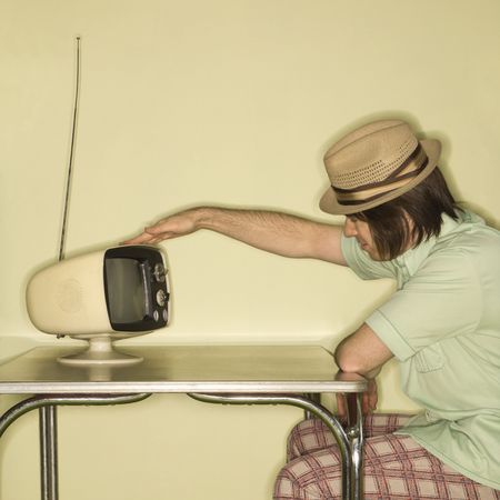 Side view of Caucasian mid-adult man wearing hat sitting at 50's retro dinette set tapping old...