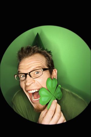 Vignette of excited adult Caucasian man on green background wearing Saint Patricks Day hat and holding shamrock.の写真素材