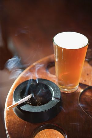 Full beer glass and cigarette with smoke rising in nightclub.の写真素材