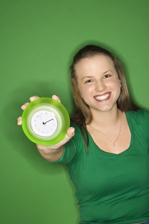 Caucasian young female adult holding out clock and smiling.の写真素材
