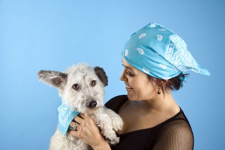 Hispanic mid-adult woman holding small white dog wearing matching bandanas.の写真素材
