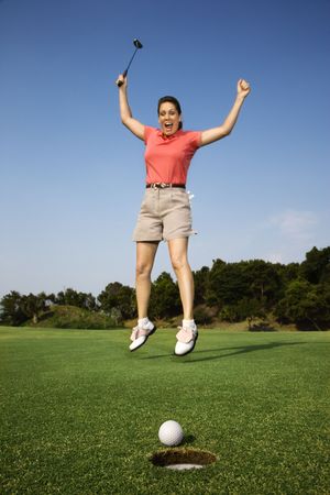 Woman holding golf club jumping in air cheering on golf course.の写真素材