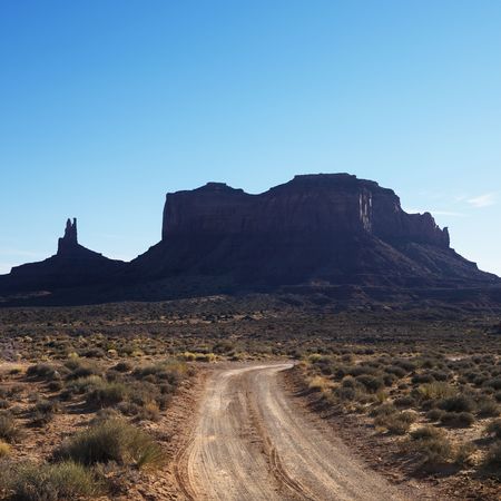 Dirt road headed toward rock formations in desert of Monument Valley, Utah.の写真素材
