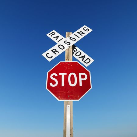 Railroad crossing and stop signs against blue sky.の写真素材