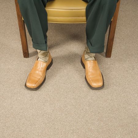Close up of man sitting in chair wearing retro pants and shoes.の写真素材