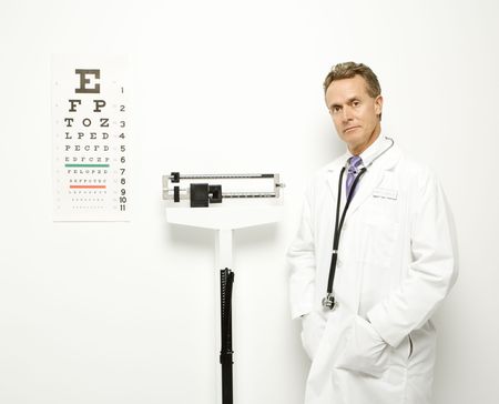 Mid-adult Caucasian male doctor standing next to scale with eye chart on wall.の写真素材