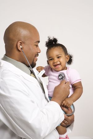 African-American male pediatrician holding and examinating baby girl with stethoscope.の写真素材