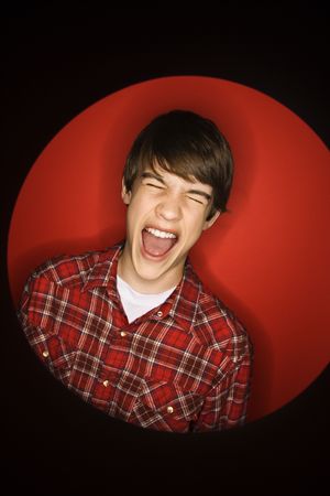 Portrait of Caucasian teen boy screaming with eyes closed against red background.の写真素材