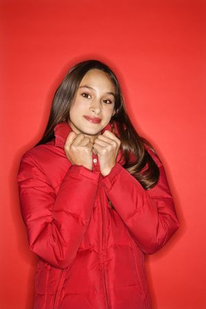 Portrait of Asian-American teen girl holding collar of her coat and smiling standing against red background.の写真素材