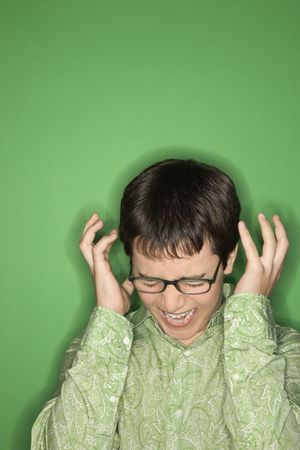 Portrait of Caucasian teen boy screaming with hands beside ears in front of green background.の写真素材