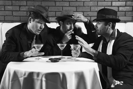Three Caucasian prime adult males in retro suits sitting at table drinking and smoking and talking.の写真素材