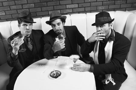 Three Caucasian prime adult males in retro suits sitting at table with cocktails looking at viewer.の写真素材