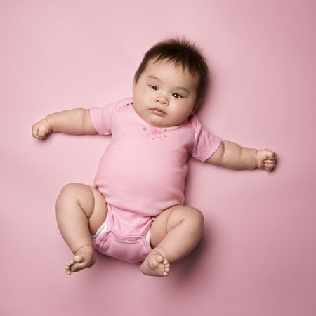 Asian baby lying on back lookin up at viewer with arms out to side.