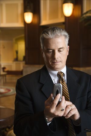 Caucasian prime adult male businessman dialing cellphone in hotel lobby.の写真素材