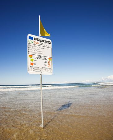 Sign and flag on beach in Surfers Paradise, Australia with lifeguard schedule.の写真素材