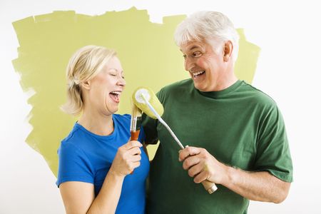 Middle-aged couple painting wall green playing with paint utensils.の写真素材