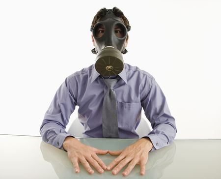 Businessman sitting in white room wearing gas mask.の写真素材
