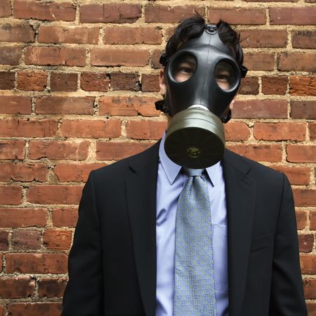 Businessman standing next to brick wall wearing gas mask.の写真素材