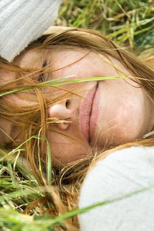 Close up portrait of attractive young redheaded woman lying in grass resting.の写真素材