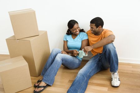 African American male and female couple sitting on floor next to moving boxes relaxing.