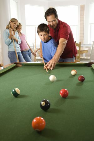 Man and boy playing pool with woman and girl in background. Vertically framed shot.の写真素材