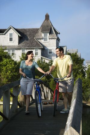 Smiling couple walking bikes across a bridge.  Vertical shot.の写真素材