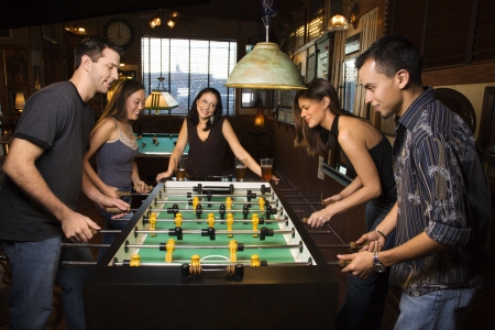 Group of young men and women enjoying a game of foosball in a bar.  Horizontal shot.