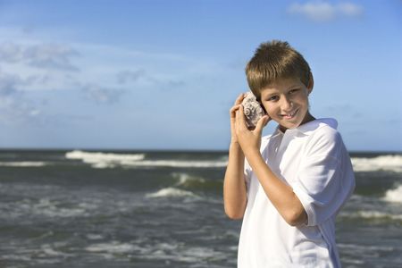 Boy listens to a shell at the beach. Horizontal shot.の写真素材