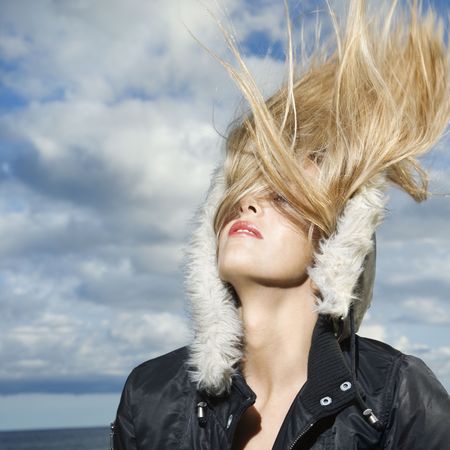 Attractive young woman is wearing a parka at the beach and flipping her long blond hair back. Square format.の写真素材